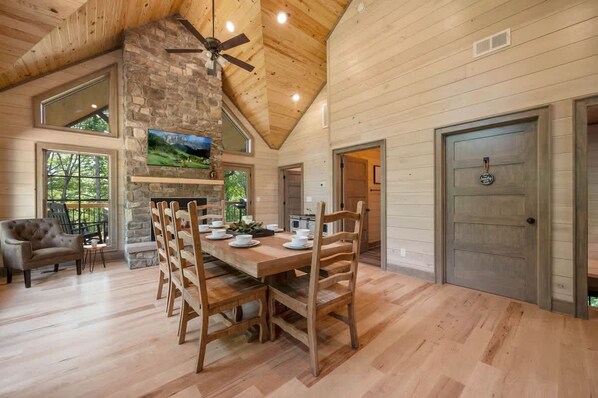 A spacious dining area with a wooden table and chairs, a stone fireplace, and a ceiling fan. - Lux Cabin, Hot Tub, Arcade, In and Out Fireplaces (Sevierville)