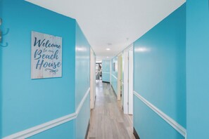 A hallway with light blue walls and a wooden floor, leading to a room with a bed and a chair. - Wonderful 3  bedroom Unit at Sand Dunes Resort (Myrtle Beach)