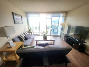 Ein modernes Wohnzimmer mit einer Couch, einem Couchtisch, einem Fernseher und einem großen Fenster mit Blick auf die Stadt.