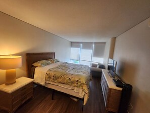 A bedroom with a bed, bedside table, lamp, dresser, and a TV. - 2-bedroom condo in soothing Honolulu with AC and fitness room (Honolulu)