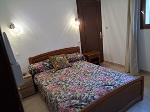 Ein Schlafzimmer mit einem hölzernen Bett, floraler Bettwäsche, Nachttischen, einem Kleiderschrank und einer Wandleuchte.