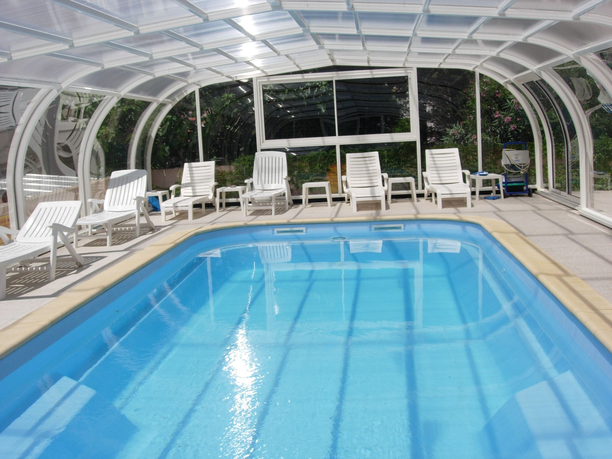 An indoor swimming pool with white lounge chairs and a glass ceiling.