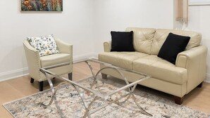 A living room with a beige sofa, a white armchair, a glass coffee table, a floral rug, and a painting of flowers on the wall. - Self-Contained, Full Kitchen, Full Bath, Private-A (Richmond Hill)