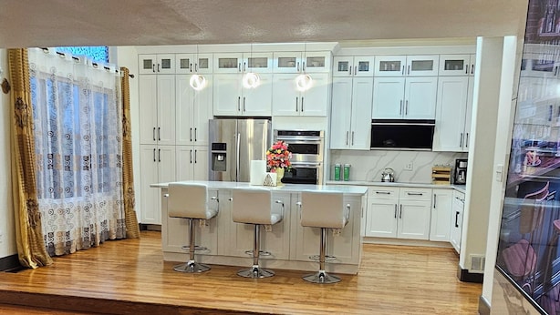 Een moderne keuken met witte kasten, een centraal eiland met barstoelen en een ingebouwde oven.