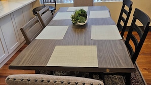 Een eethoek met een houten tafel, stoelen, een planten decoratie en uitzicht door grote ramen.