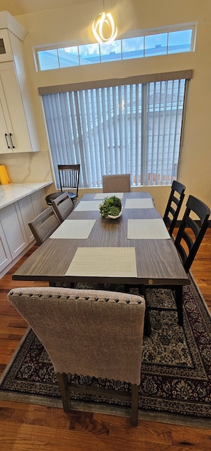 Un espace repas avec une table en bois, des chaises, un arrangement floral en guise de centre de table et une vue dégagée grâce à de grandes fenêtres.