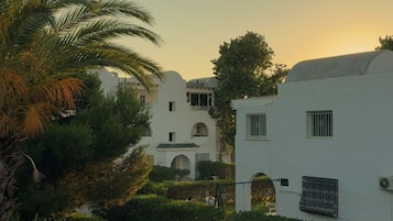 A courtyard with white buildings, palm trees, and a clear sky.