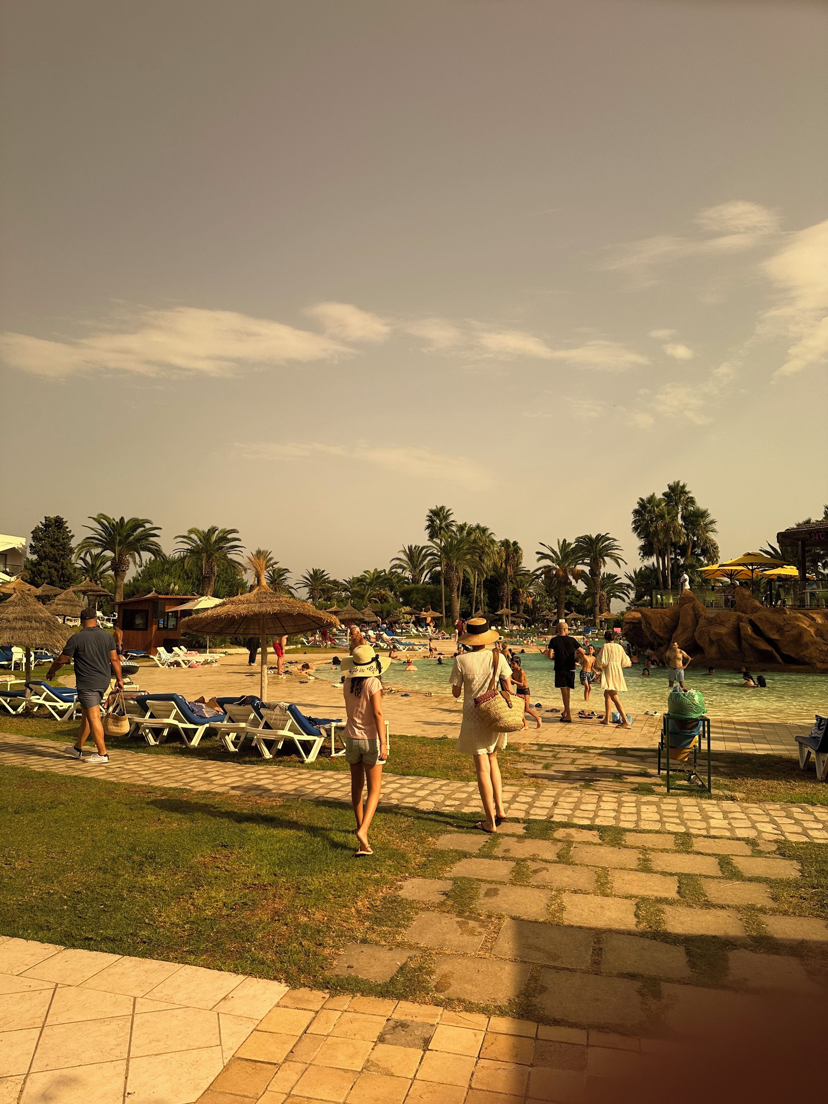 Ein Strandhotel mit Liegestühlen, Palmen und einem Poolbereich.