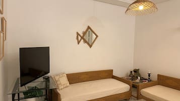 A living room with a sofa, a glass coffee table, a television on a stand, and a decorative mirror on the wall.