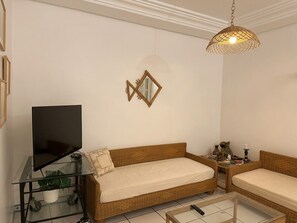 Un salon comprenant un canapé, une table basse en verre, un téléviseur posé sur un meuble et un miroir décoratif accroché au mur.