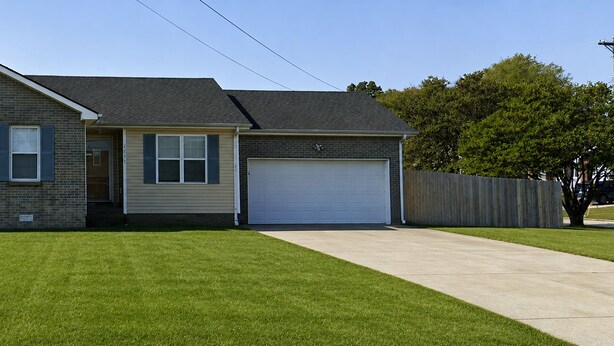 A two-story house with a garage, a well-maintained lawn, and a wooden fence. - 3BR/2BA Near Fort Campbell & Tennova - Fenced Yard, Pet Friendly, Back Patio (Clarksville)