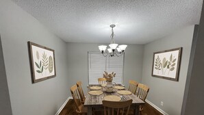 A dining room with a wooden table, chairs, a chandelier, and framed botanical artwork on the walls. - 3BR/2BA Near Fort Campbell & Tennova - Fenced Yard, Pet Friendly, Back Patio (Clarksville)