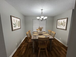 Ein Esszimmer mit Holztisch, Stühlen, einer Chandelüster und gerahmten botanischen Kunstwerken an den Wänden.