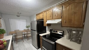 A kitchen with wooden cabinets, a stainless steel refrigerator, a black oven, and a dining area with a table and chairs. - 3BR/2BA Near Fort Campbell & Tennova - Fenced Yard, Pet Friendly, Back Patio (Clarksville)