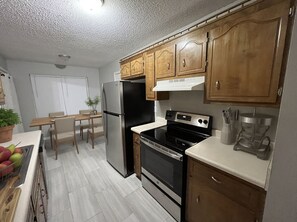 Eine Küche mit Holzausbau, einem Edelstahlkühlschrank, einem schwarzen Ofen und einem Essbereich mit Tisch und Stühlen.