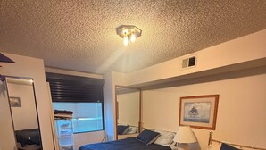 Ein Schlafzimmer mit zwei Betten, einem Schreibtisch, einem Stuhl, einem Kleiderschrank und einem Fenster mit Jalousien.