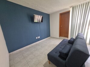 Una sala de estar con pared azul, un televisor de pantalla plana montado en ella, un sofá de color oscuro y una puerta de madera.
