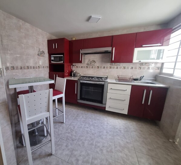 Una cocina con armarios rojos, una encimera blanca, una estufa, un horno y un fregadero.