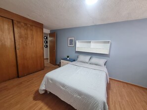 Un dormitorio con cama, armario, mesita de noche y estante en la pared.