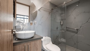 Un baño moderno con tocador de mármol, inodoro, cabina de ducha de vidrio y un espejo grande.