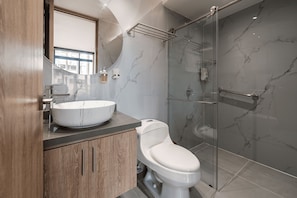 Ein modernes Badezimmer mit Marmorwaschtisch, Toilette, Duschkabine aus Glas und großem Spiegel.