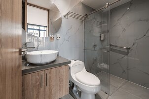 Un baño moderno con tocador de mármol, inodoro, cabina de ducha de vidrio y un espejo grande.