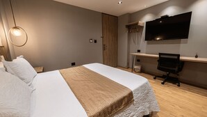 Un dormitorio moderno con cama, escritorio, silla y televisor en la pared.