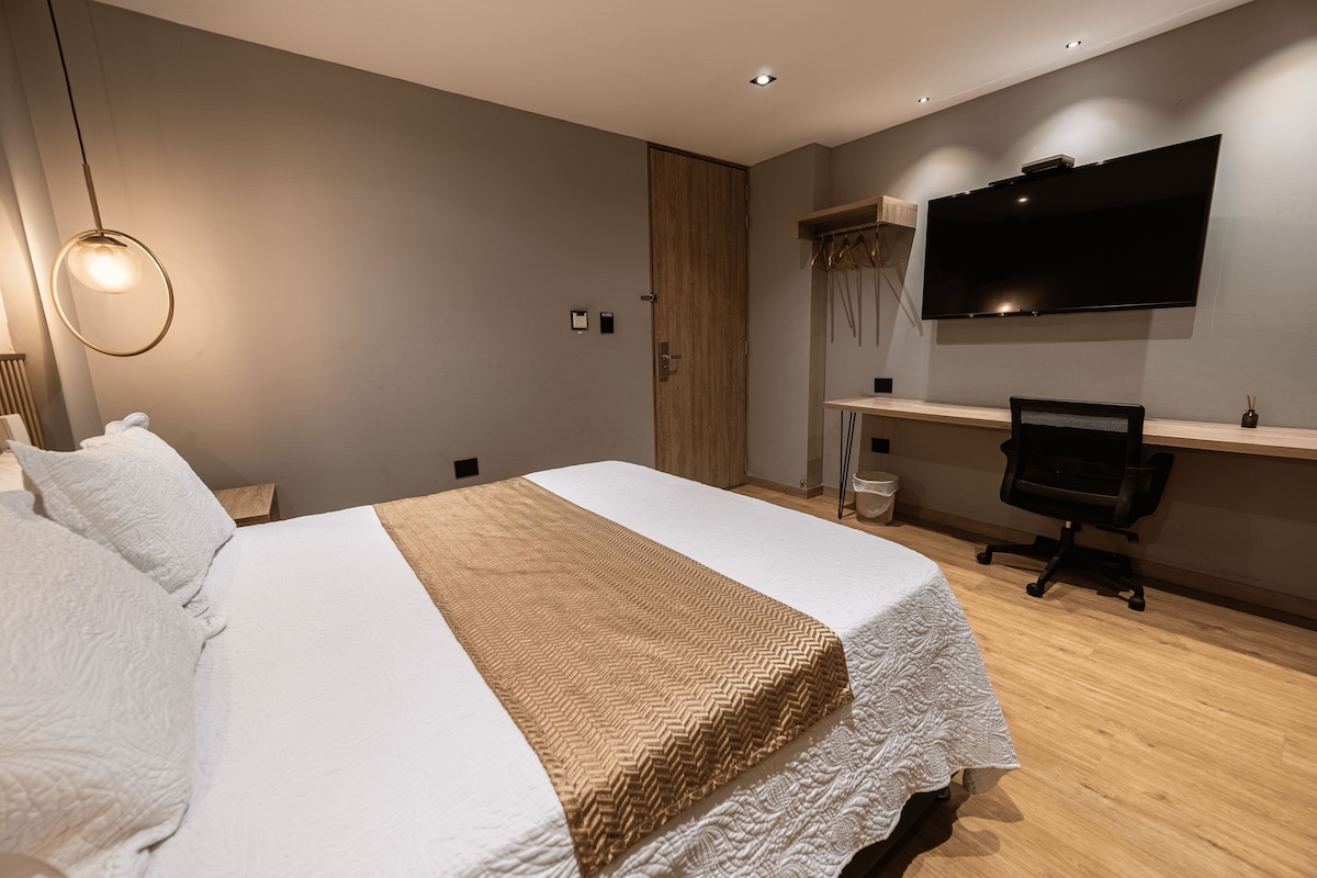 Un dormitorio moderno con cama, escritorio, silla y televisor en la pared.