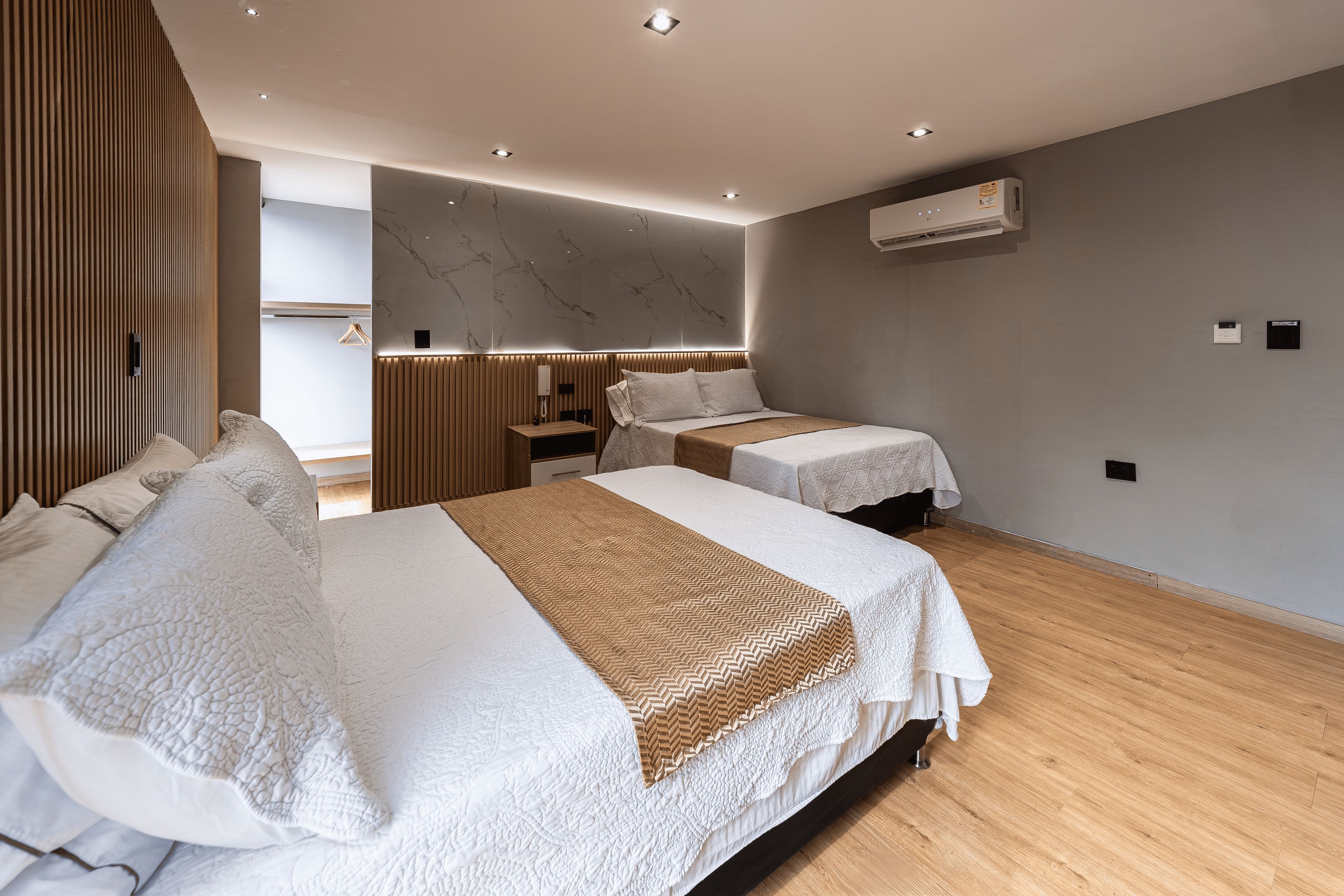 Una habitación de hotel moderna con dos camas, piso de madera, pared de mármol y unidad de aire acondicionado.