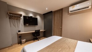 Una habitación de hotel moderna con cama, escritorio, silla y televisor montado.