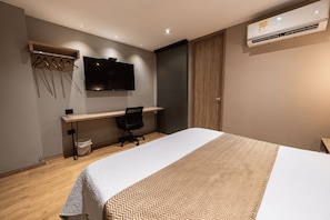 Ein modernes Hotelzimmer mit Bett, Schreibtisch, Stuhl und einem an der Wand befestigten Fernseher.