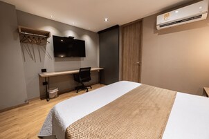 Una habitación de hotel moderna con cama, escritorio, silla y televisor montado.