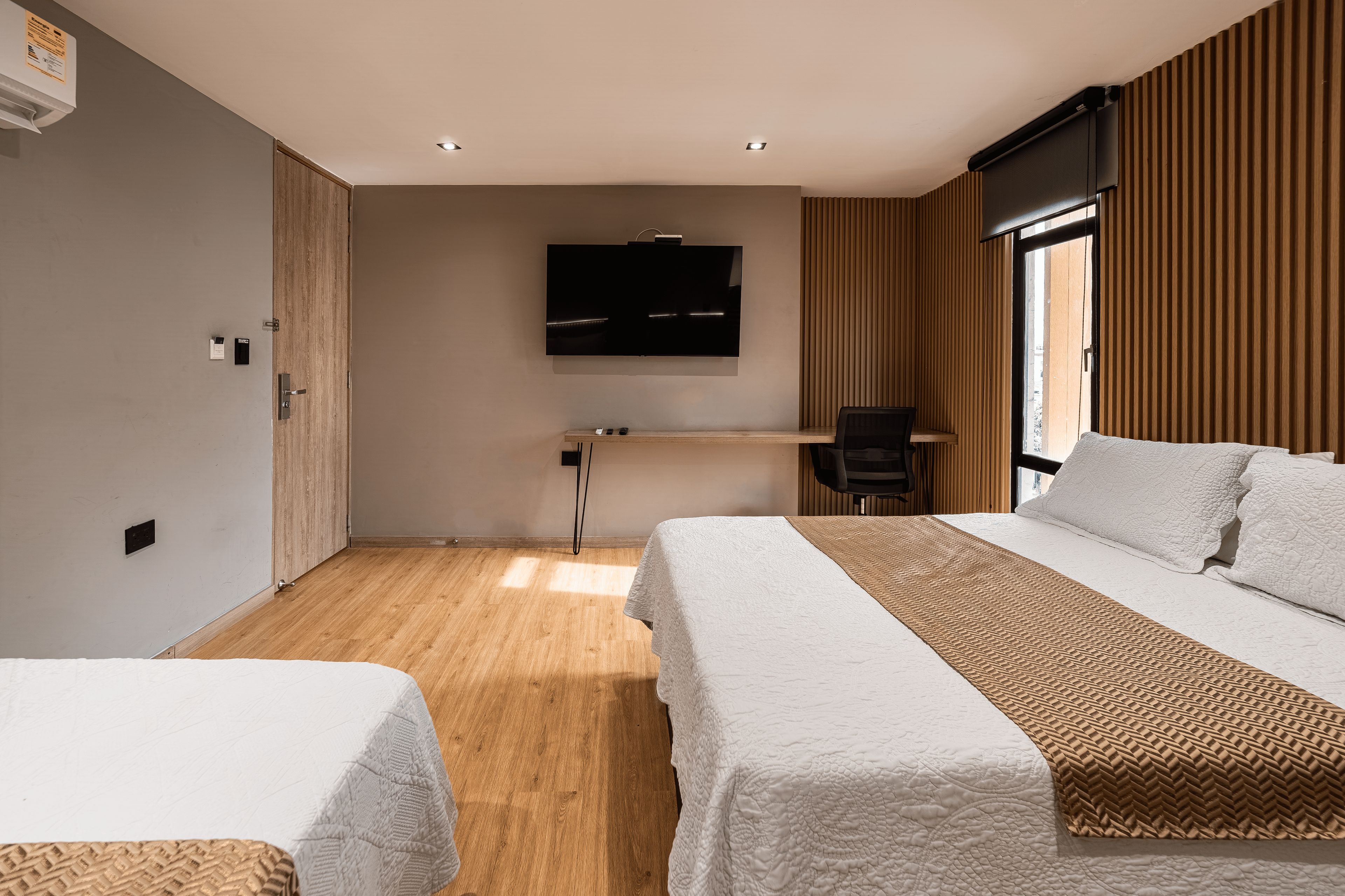 Een hotelkamer met twee bedden, een bureau, een televisie en een raam met zonwering.