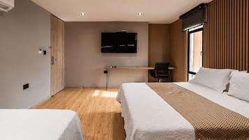 Een hotelkamer met twee bedden, een bureau, een televisie en een raam met zonwering.