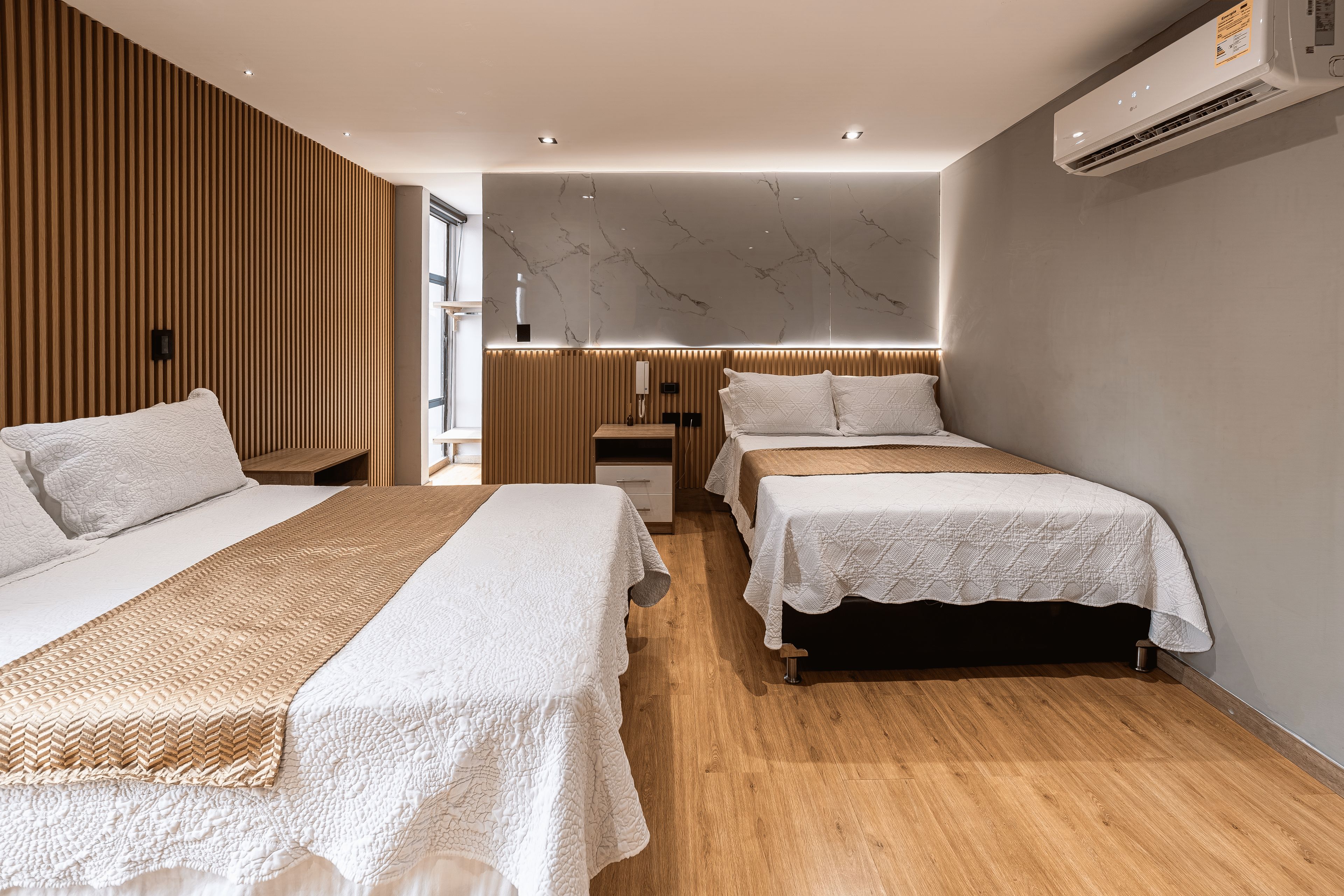 Moderni hotellihuone, jossa on kaksi sänkyä, puupanelointi, marmoriseinä ja ilmastointilaite.