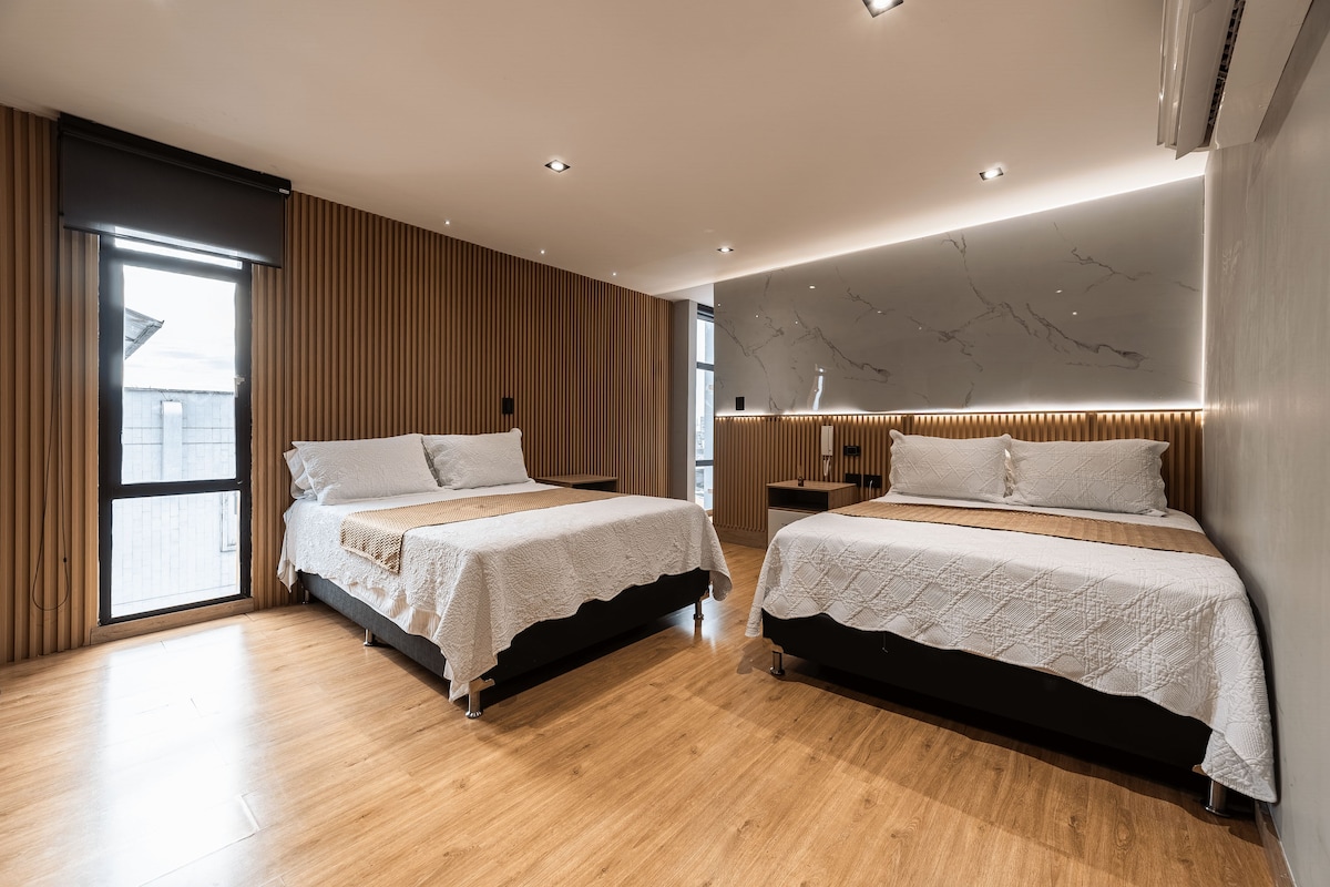Una habitación de hotel moderna con dos camas, piso de madera y un ventanal grande.
