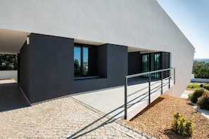 A modern building with a flat roof, large windows, and a concrete pathway leading to a metal staircase. - Heading South Private Oasis (Quarteira)
