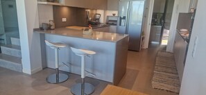 A modern kitchen with a central island, two bar stools, a refrigerator, and a countertop with a coffee machine. - Heading South Private Oasis (Quarteira)