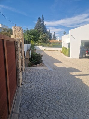 A paved driveway leading to a modern house with a stone wall and a wooden gate. - Heading South Private Oasis (Quarteira)