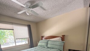 Ein Schlafzimmer mit einem Bett, einem Deckenventilator, einem Fenster mit Jalousien und einem karierten Teppich.