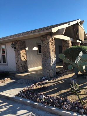 Een huis met een gevel van natuursteen, een overdekte veranda en een cactus in de voortuin.