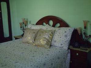 A bed with a floral patterned bedspread, two pillows with gold and white patterns, and a wooden headboard.