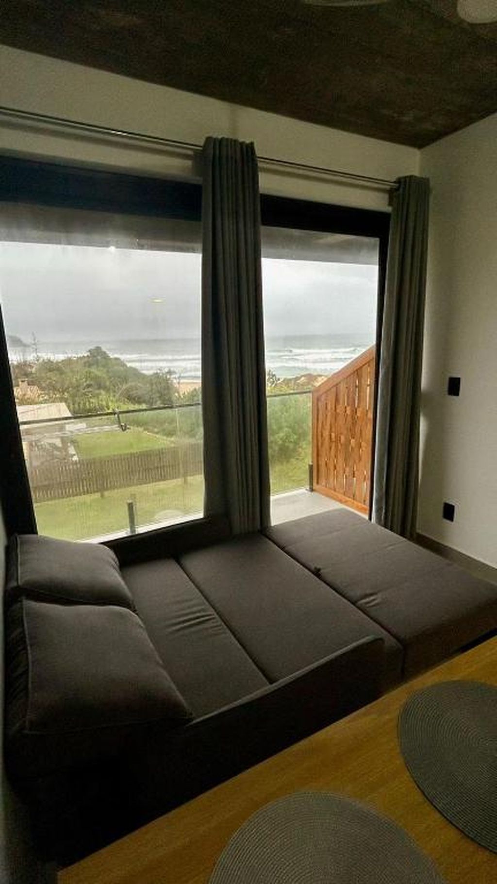 Quarto moderno com uma janela grande, um sofá e vista para uma paisagem verde.