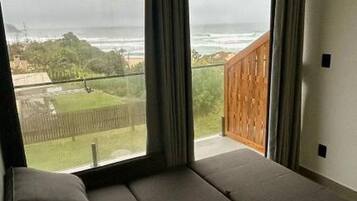Quarto moderno com uma janela grande, um sofá e vista para uma paisagem verde.