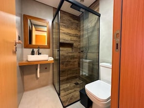 A modern bathroom with a glass shower enclosure, a wooden vanity, and a toilet. - Casa Oceano - Praia do Rosa (Imbituba)