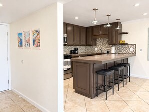 A modern kitchen with a central island, bar stools, and a tiled backsplash. - Cute San Clemente 1BDRM Condo - Minutes To Beach (San Clemente)