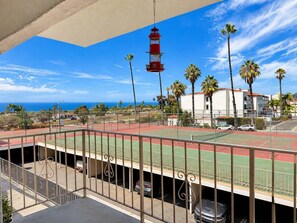 A tennis court with a red and green surface, a red lighthouse in the background, and palm trees. - Cute San Clemente 1BDRM Condo - Minutes To Beach (San Clemente)