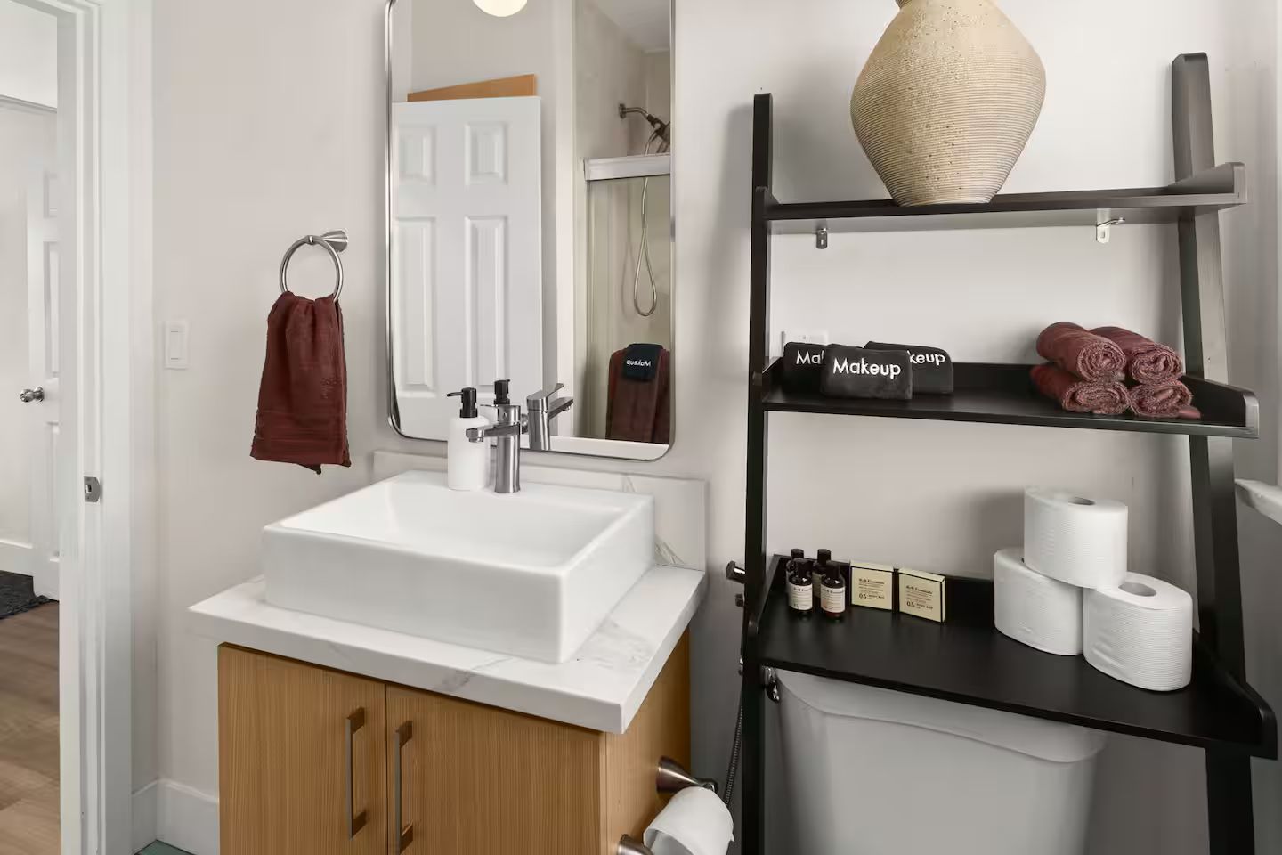 Une salle de bain avec un lavabo blanc, un miroir, un porte-serviettes, une étagère avec des articles de toilette et un espace douche.