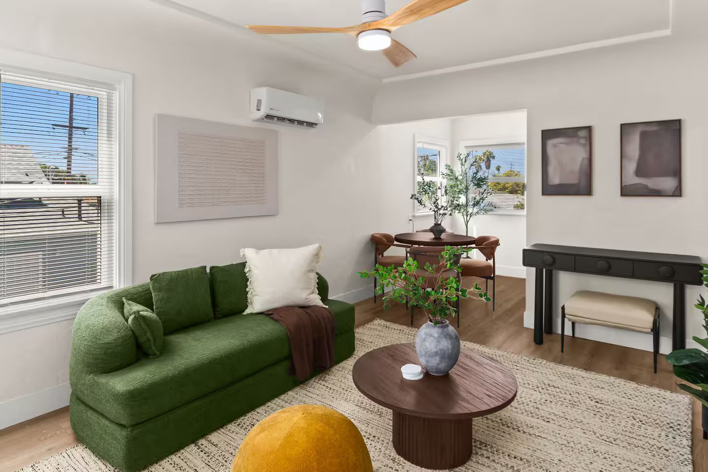 A modern living room with a green sofa, a round coffee table, and a dining area with a table and chairs.