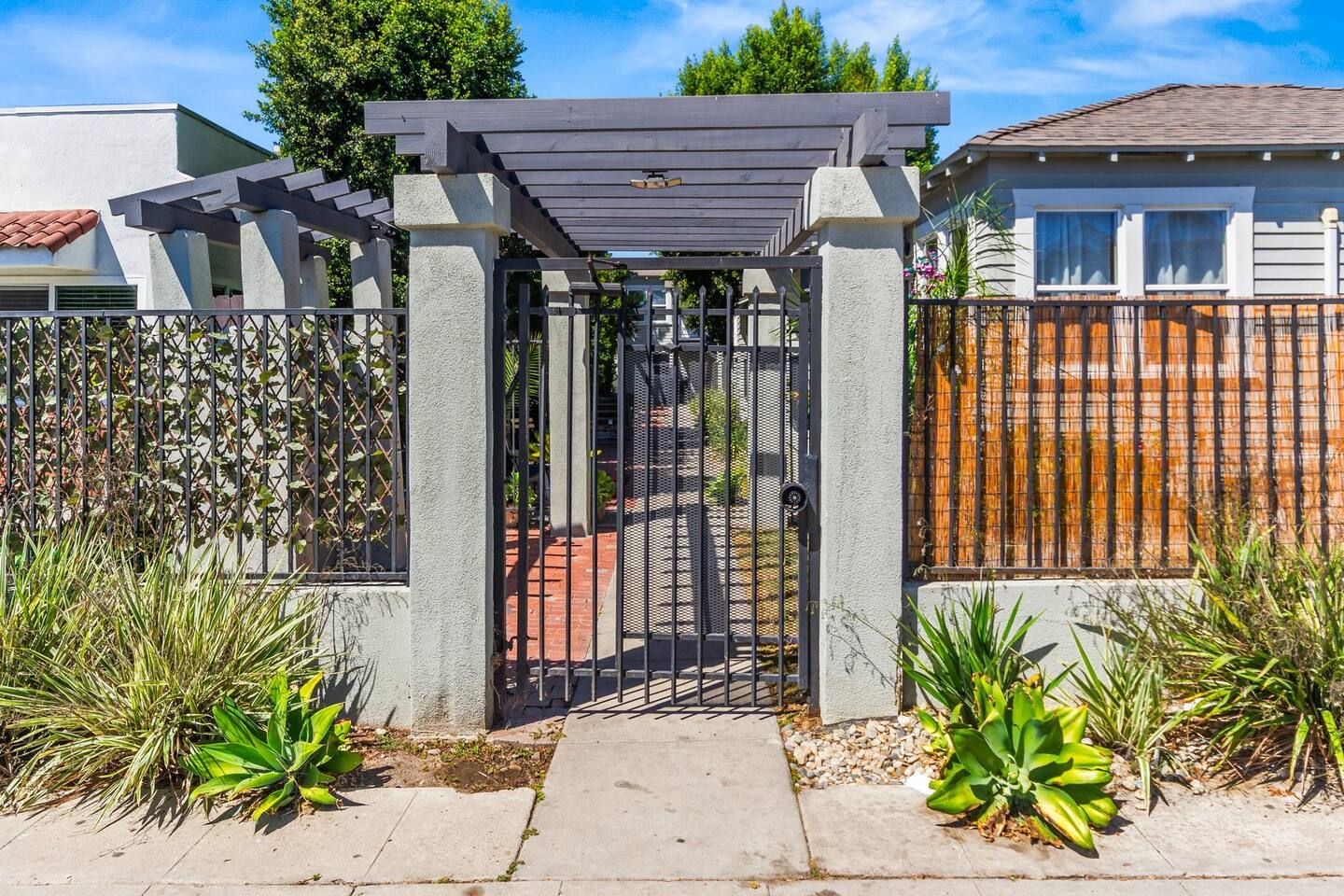 A gated entrance with a pergola, a concrete pathway, and a fence with climbing plants.